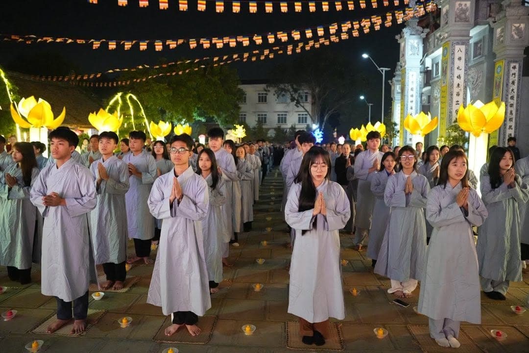 Phật tử áo tràng chắp tay bên đèn hoa sen trong lễ cầu an ban đêm tại Chùa Pháp Vân