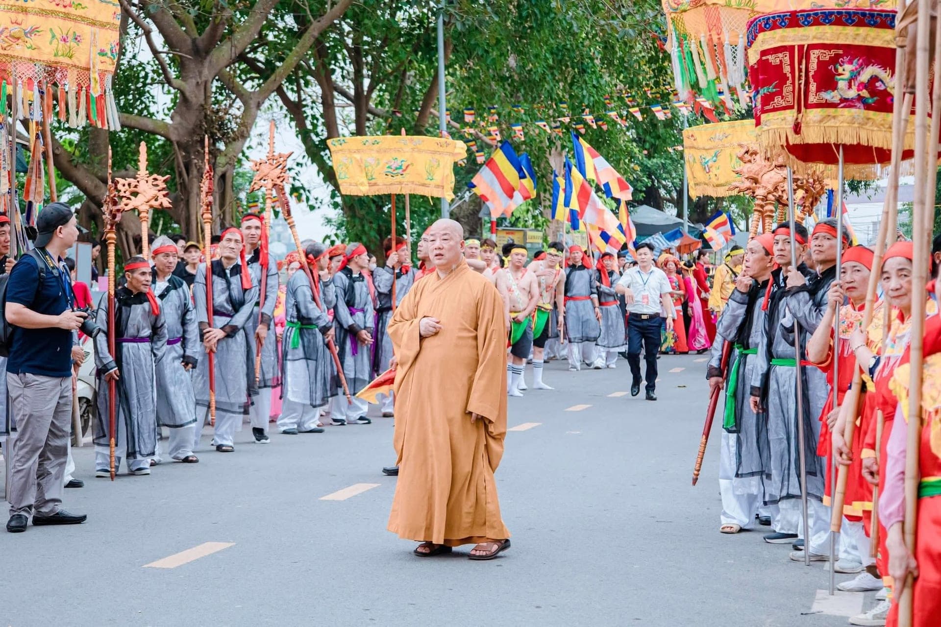 Sư trụ trì khoác áo cà sa vàng đi giữa hai hàng người cầm lọng và cờ lễ